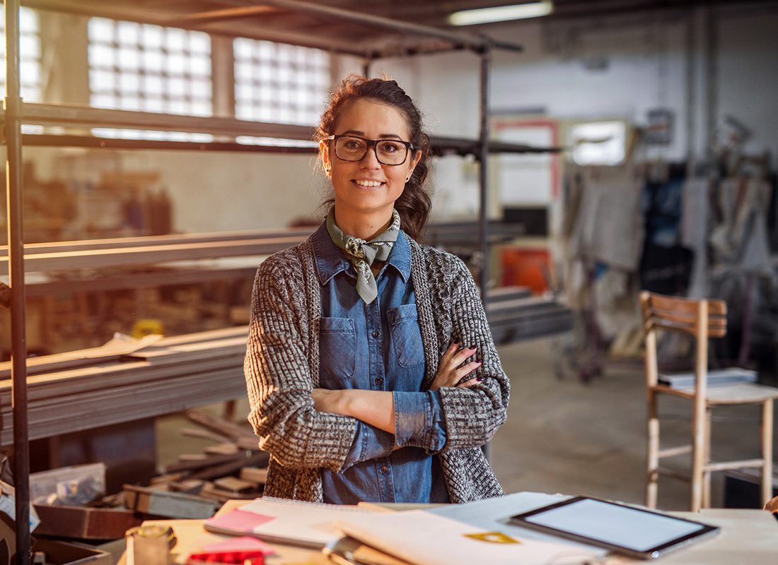 Business Insurance - Portrait of a Smiling Middle Aged Female Engineer Standing in Front of a Table with a Tablet and Papers with Construction Equipment in the Background
