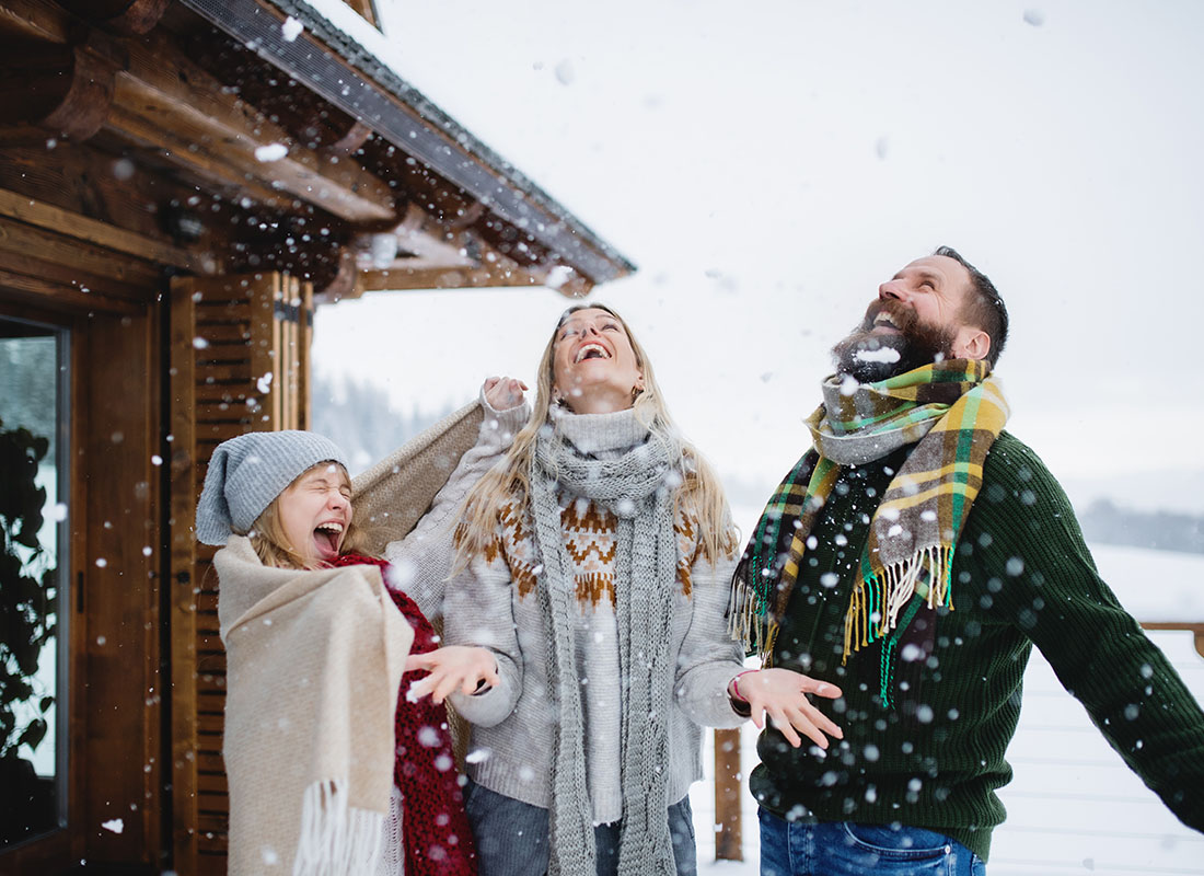 Contact - Portrait of an Excited Family with an Older Daughter Wearing Sweaters Having Fun Standing Outside on the Deck of a Wooden House Watching the Snow Fall