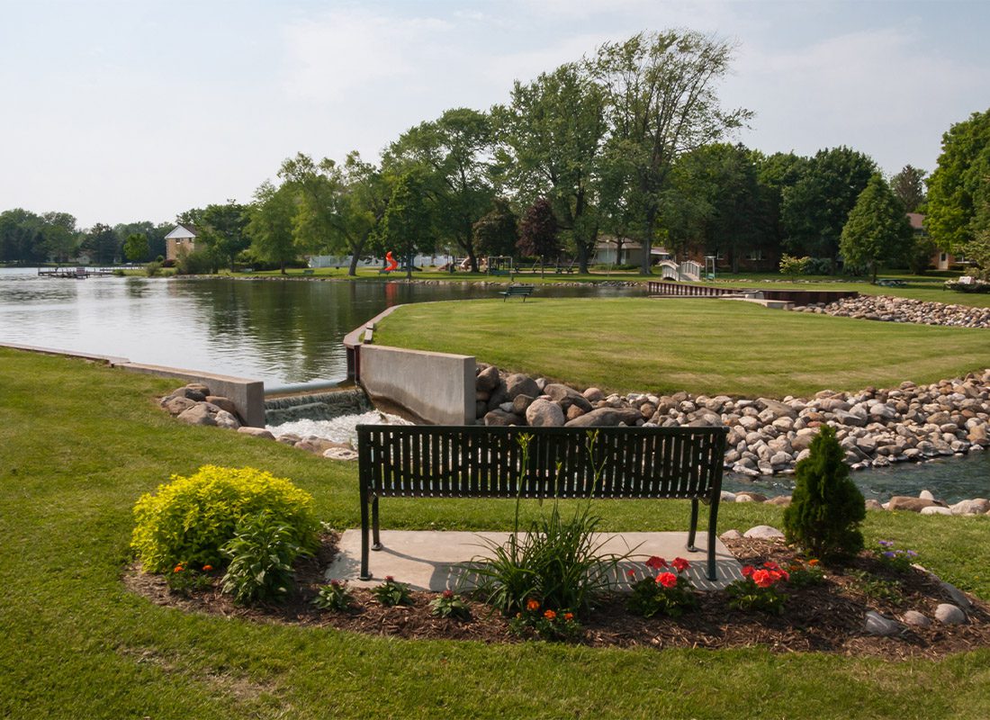 Schofield, WI - Scenic Shot of a Park Bench by a Small Lake in a Park in Wisconsin